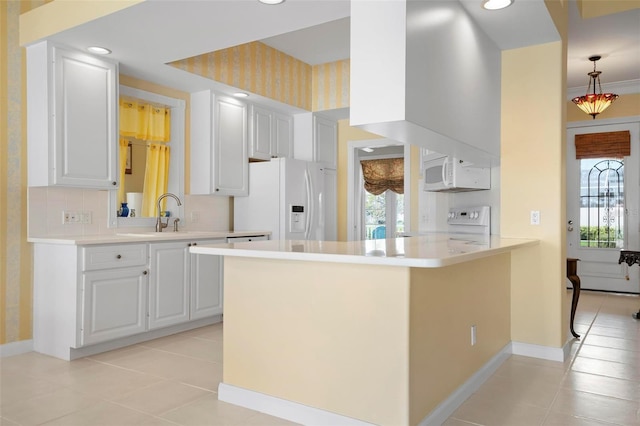 kitchen with white appliances, a peninsula, light countertops, white cabinetry, and a wealth of natural light