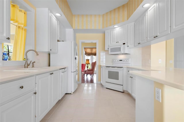 kitchen with white appliances, wallpapered walls, light countertops, white cabinetry, and a sink