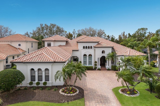 mediterranean / spanish house featuring stucco siding, a front yard, decorative driveway, and a tiled roof