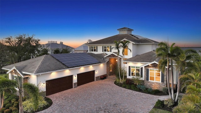 view of front of house featuring a tile roof, solar panels, an attached garage, stone siding, and driveway