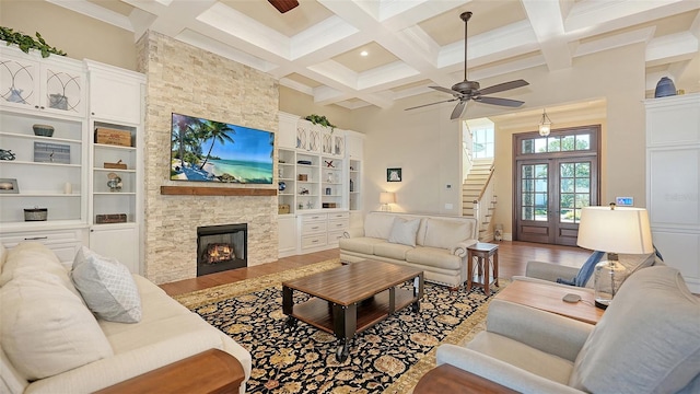 living room featuring a stone fireplace, beamed ceiling, a towering ceiling, and wood finished floors