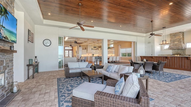 living area featuring wooden ceiling, brick floor, a tray ceiling, a stone fireplace, and recessed lighting