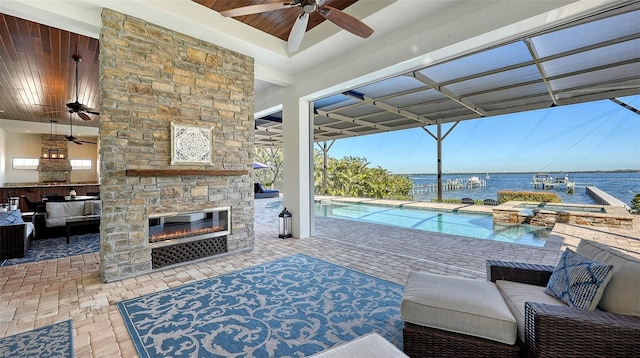 interior space with a water view, a pool with connected hot tub, ceiling fan, and an outdoor stone fireplace