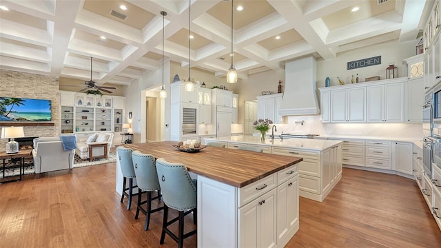 kitchen with custom exhaust hood, a spacious island, visible vents, a high ceiling, and butcher block countertops