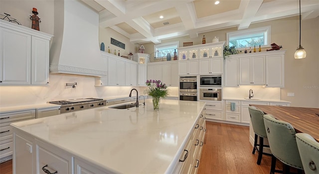 kitchen featuring a high ceiling, coffered ceiling, a sink, appliances with stainless steel finishes, and custom range hood