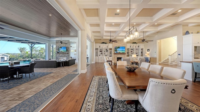 dining area featuring a large fireplace, coffered ceiling, ceiling fan, beamed ceiling, and wood finished floors