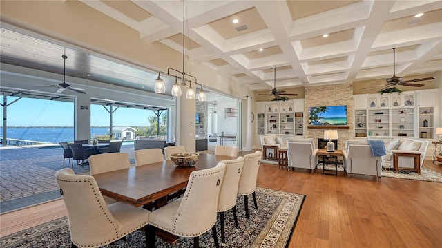 dining space with beam ceiling, visible vents, a water view, and wood finished floors