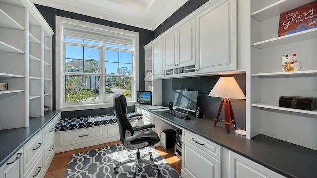 office with built in desk, wood finished floors, and crown molding