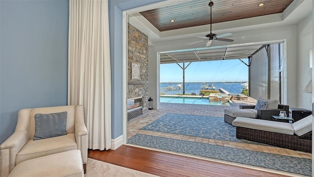 living area with wooden ceiling, a water view, wood finished floors, a sunroom, and a raised ceiling