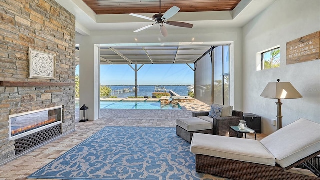 living area with brick floor, a tray ceiling, a sunroom, and a water view