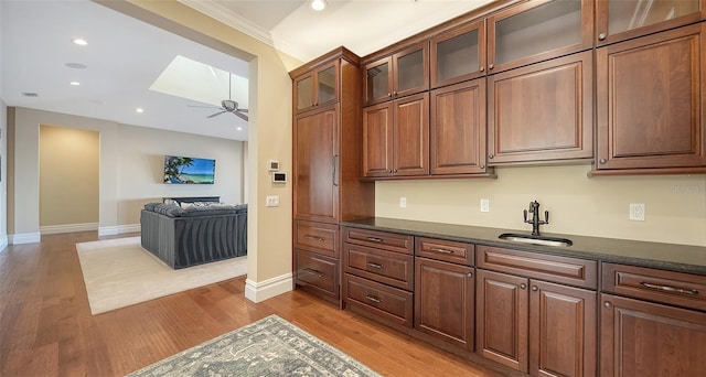 kitchen featuring recessed lighting, a skylight, wood finished floors, a sink, and dark countertops