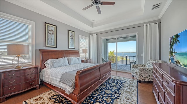 bedroom featuring dark wood-style flooring, a raised ceiling, visible vents, ornamental molding, and access to outside