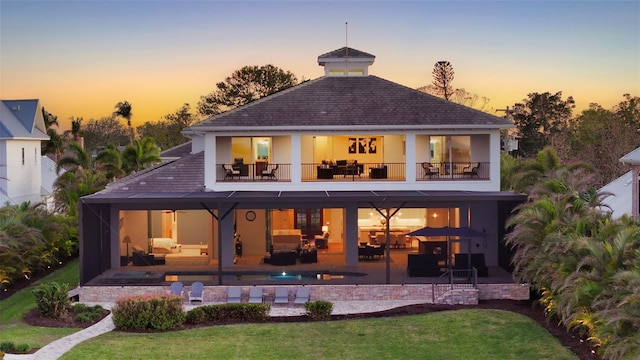 back of house at dusk featuring outdoor dining area, an outdoor living space, a patio, and a balcony