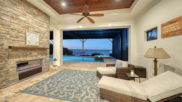 living area with a raised ceiling, wooden ceiling, a sunroom, ceiling fan, and a fireplace