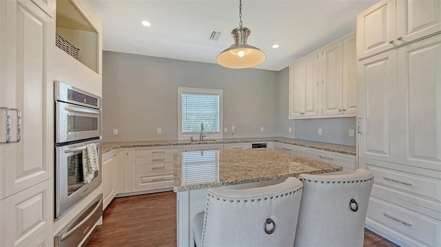 kitchen with dark wood finished floors, visible vents, stainless steel double oven, a kitchen island, and a sink