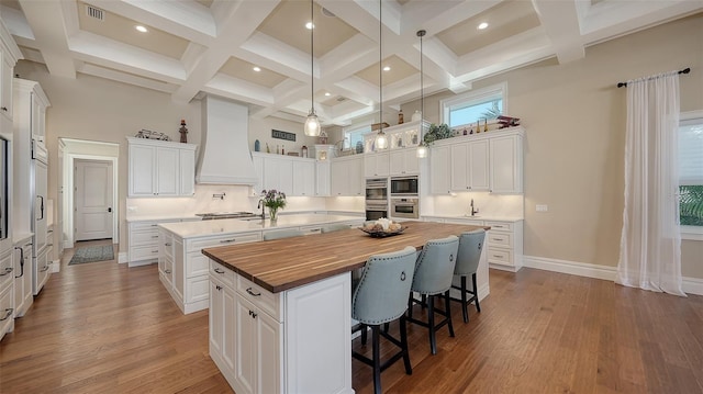 kitchen with premium range hood, a high ceiling, wooden counters, appliances with stainless steel finishes, and a large island