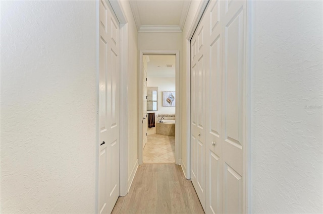 hallway featuring a textured wall, ornamental molding, and light wood-style flooring