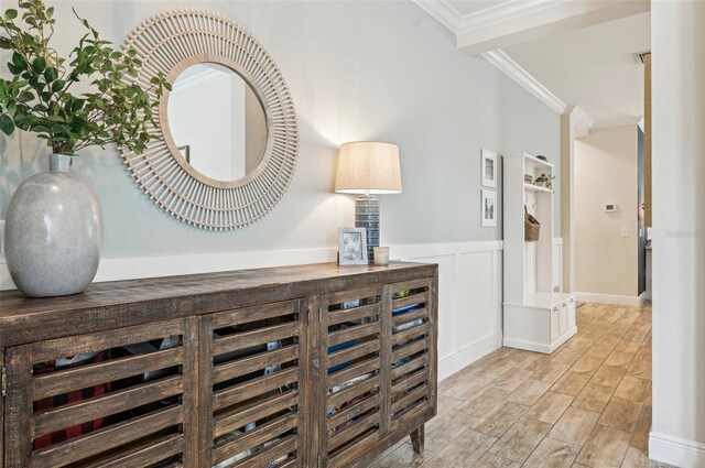 interior space featuring wainscoting, a decorative wall, crown molding, and wood finished floors