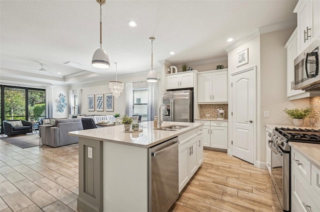 kitchen featuring a center island with sink, open floor plan, stainless steel appliances, white cabinetry, and pendant lighting