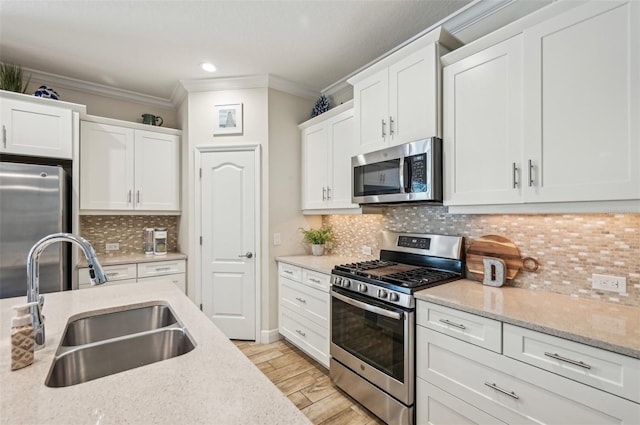 kitchen featuring appliances with stainless steel finishes, ornamental molding, white cabinets, a sink, and light wood-type flooring