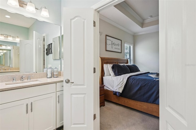 bedroom with light colored carpet, a sink, a tray ceiling, ensuite bath, and crown molding