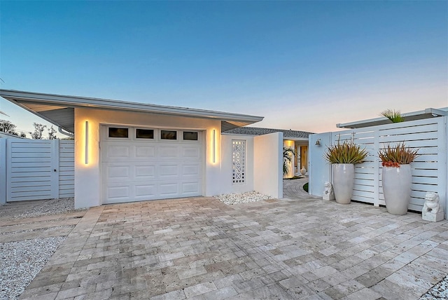 view of front of property with a garage, decorative driveway, fence, and stucco siding