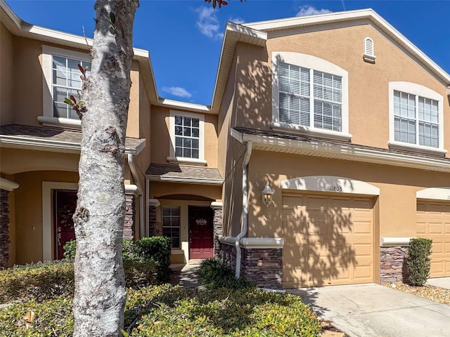 multi unit property with a garage, stone siding, concrete driveway, and stucco siding