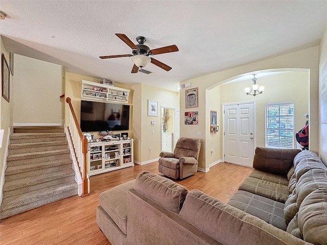 living area with arched walkways, light wood-style flooring, stairs, a textured ceiling, and ceiling fan with notable chandelier