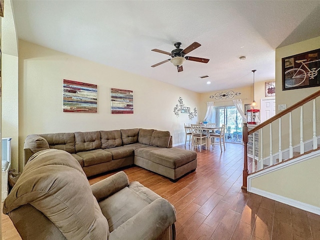 living area featuring visible vents, a ceiling fan, wood finished floors, baseboards, and stairs