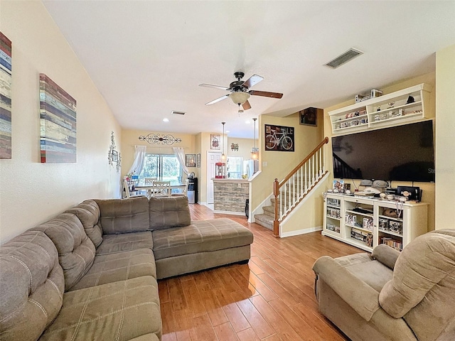 living area featuring ceiling fan, wood finished floors, visible vents, baseboards, and stairway