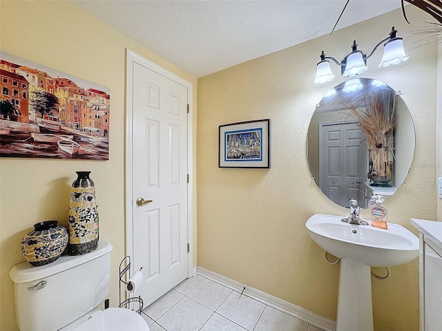 half bathroom with a textured ceiling, tile patterned flooring, toilet, baseboards, and a closet