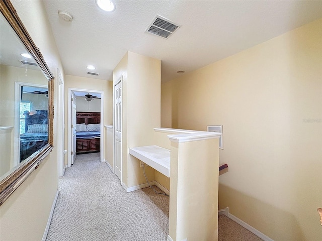 hall with baseboards, visible vents, light colored carpet, and an upstairs landing