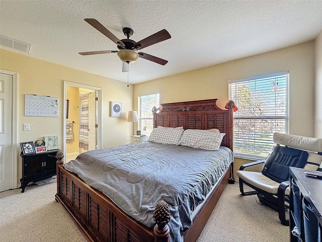 bedroom with light carpet, visible vents, ensuite bath, ceiling fan, and a textured ceiling