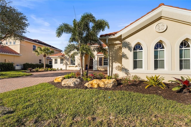 mediterranean / spanish-style home with a tiled roof, decorative driveway, a front yard, and stucco siding