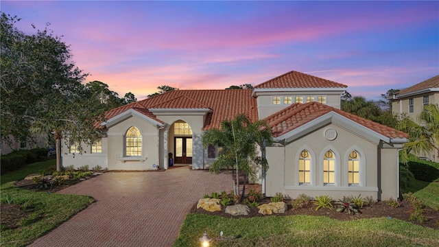 mediterranean / spanish-style house featuring a tiled roof, french doors, decorative driveway, and stucco siding