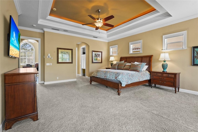 carpeted bedroom with baseboards, arched walkways, a raised ceiling, ceiling fan, and ornamental molding