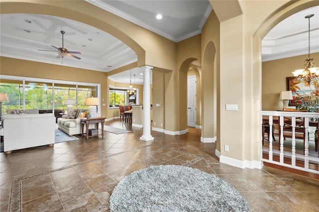 foyer with a tray ceiling, crown molding, baseboards, ornate columns, and ceiling fan with notable chandelier