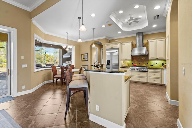 kitchen with wall chimney range hood, cream cabinets, appliances with stainless steel finishes, and a healthy amount of sunlight