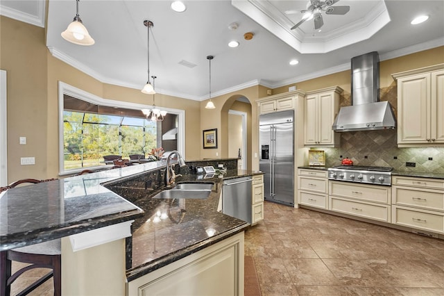 kitchen featuring appliances with stainless steel finishes, a sink, cream cabinets, and wall chimney exhaust hood