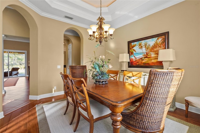 dining space with baseboards, crown molding, a tray ceiling, and wood finished floors