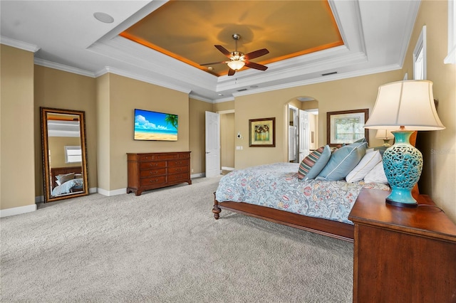 carpeted bedroom with a tray ceiling, crown molding, arched walkways, and baseboards