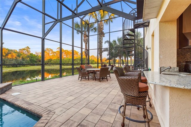 view of patio / terrace featuring a lanai, a water view, a sink, outdoor dry bar, and stairs