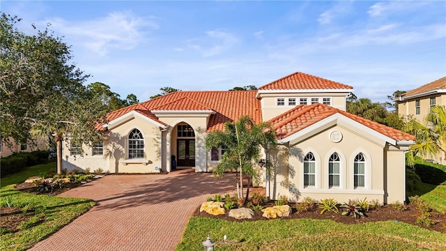 mediterranean / spanish house featuring a tiled roof, french doors, decorative driveway, and stucco siding