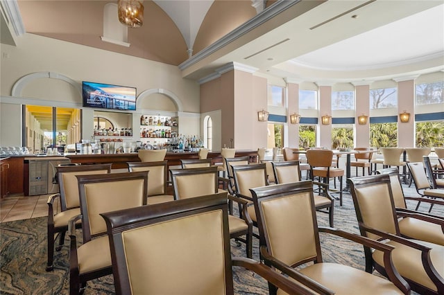 interior space featuring light tile patterned floors, high vaulted ceiling, ornamental molding, and a dry bar