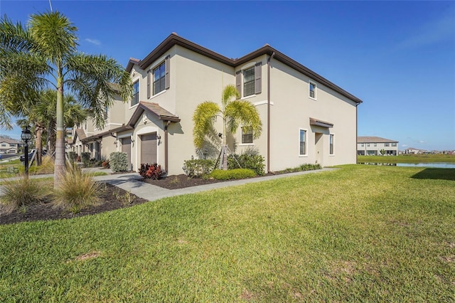 view of side of property with a water view, an attached garage, stucco siding, and a lawn