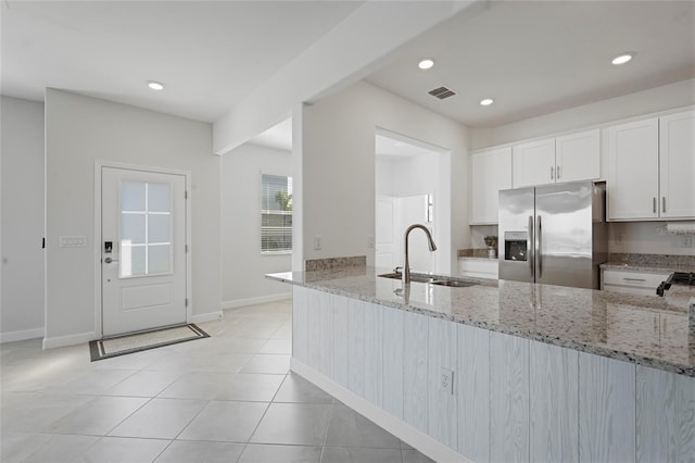 kitchen with stainless steel fridge with ice dispenser, visible vents, a sink, a peninsula, and light stone countertops