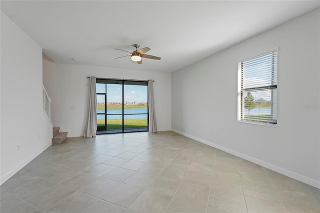 empty room featuring baseboards, stairway, light tile patterned floors, ceiling fan, and a water view