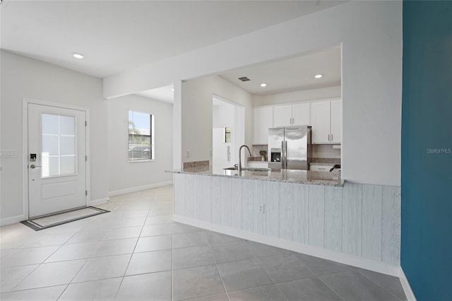 kitchen featuring light tile patterned floors, baseboards, stainless steel refrigerator with ice dispenser, white cabinetry, and light stone countertops