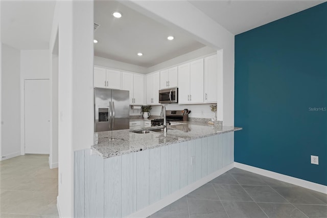 kitchen with light stone counters, tile patterned flooring, white cabinets, appliances with stainless steel finishes, and a sink