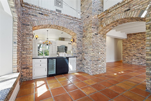 bar featuring arched walkways, a notable chandelier, a high ceiling, brick wall, and beverage cooler